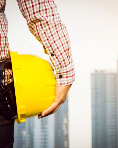 hand-s-engineer-worker-holding-yellow-safety-helmet-with-building-on-site-background